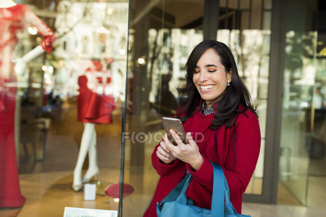 Happy woman using cell phone in front of shop window — Stock Photo