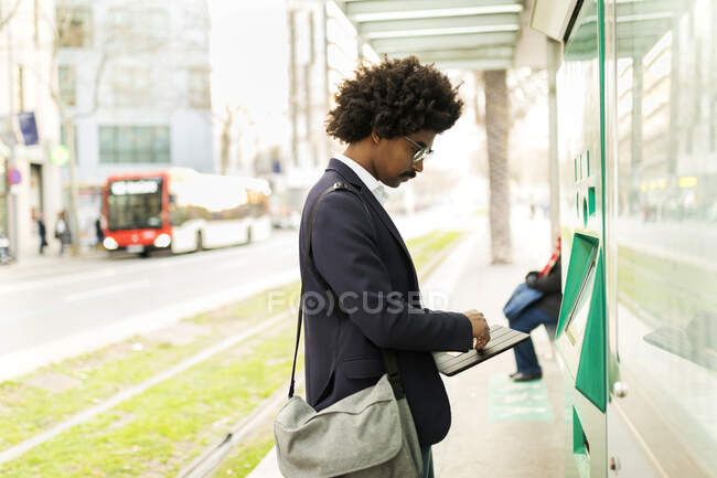 España, Barcelona, hombre de negocios utilizando la máquina expendedora de billetes en la parada de tranvía de la ciudad - foto de stock