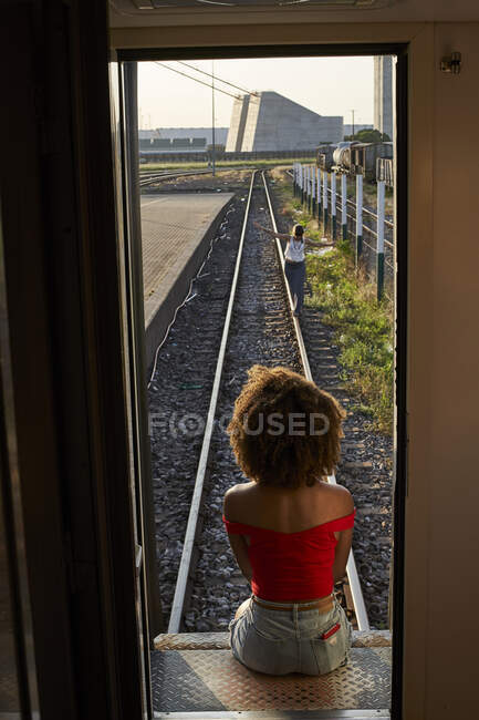 Mujer sentada en la puerta trasera de un tren mirando a una mujer en las vías - foto de stock