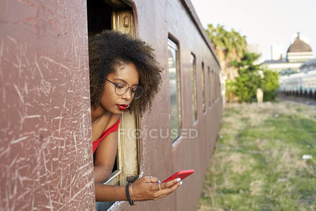 Молода жінка перевіряє телефон біля вікна поїзда — стокове фото