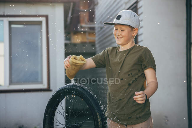 Glücklicher Junge putzt Fahrrad auf Hof — Stockfoto