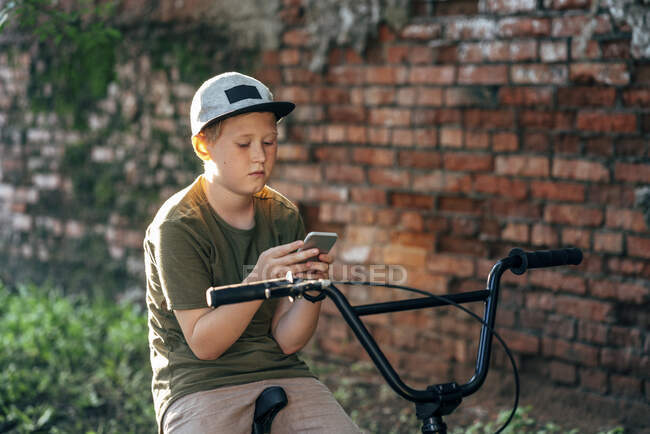 Мальчик с велосипедом bmx с помощью мобильного телефона — стоковое фото