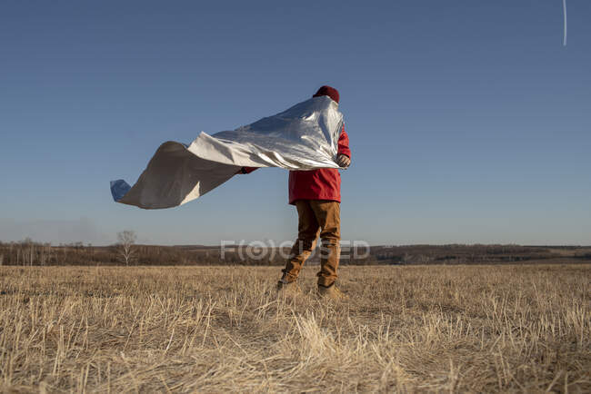 Vista trasera del niño vestido como superhéroe de pie en el paisaje de la estepa - foto de stock