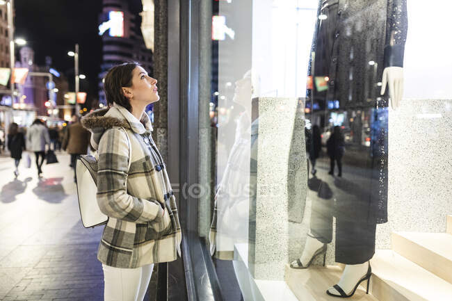 España, Madrid, joven en la ciudad por la noche junto a la Gran Vía mirando un escaparate - foto de stock