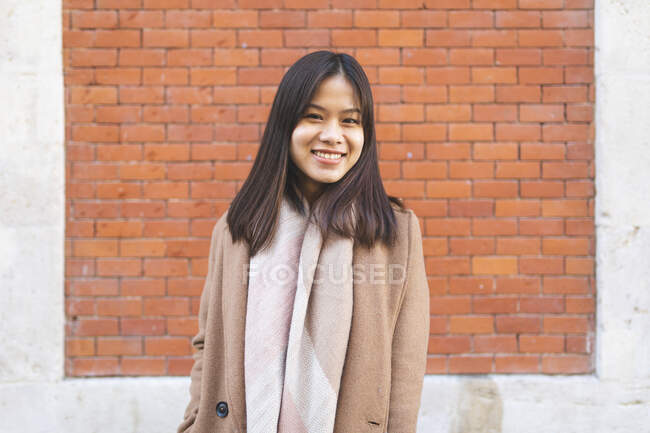 Портрет усміхненої молодої жінки біля цегляної стіни — стокове фото