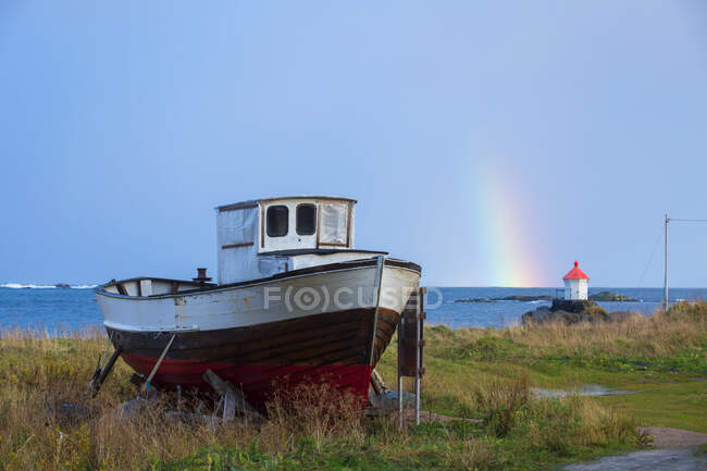 Noruega, Islas Lofoten, Eggum, barco en la costa y arco iris sobre el mar - foto de stock