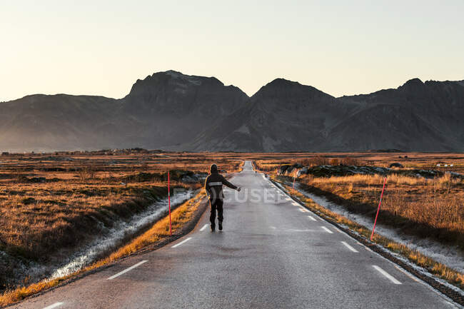 Norwegen, Lofoten, Rückansicht eines Mannes, der auf einer leeren Landstraße trampt — Stockfoto