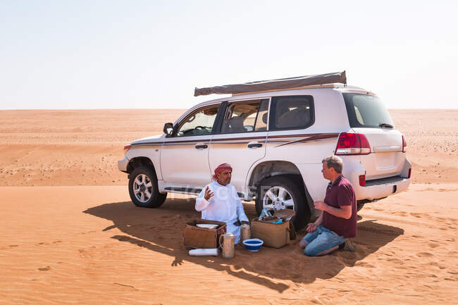 Турист делает перерыв на кофе со своим местным водителем в пустыне, Вахиба Сэндс, Оман — стоковое фото