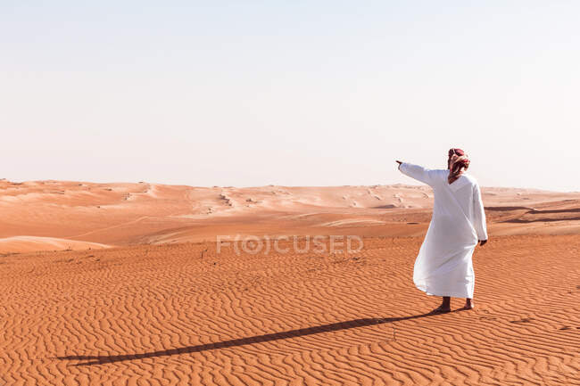Bedouin in National dress standing in the desert, pointing at distance, Wahiba Sands, Oman — Stock Photo