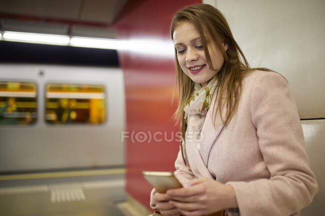 Austria, Vienna, ritratto di una giovane donna sorridente alla stazione della metropolitana che guarda lo smartphone — Foto stock