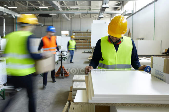 Arbeiter begutachtet Holzbretter in Fabrik, während sich Kollegen im Hintergrund bewegen — Stockfoto