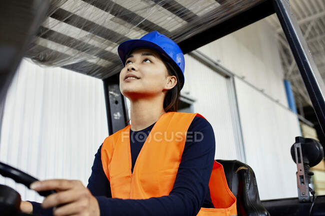 Female worker on forklift in factory looking up — Stock Photo