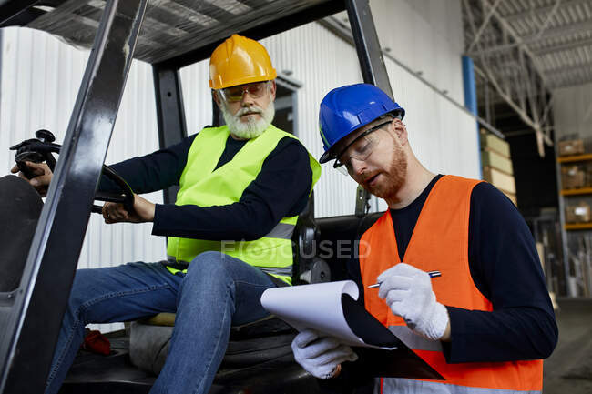 Man talking to worker on forklift in factory — Stock Photo