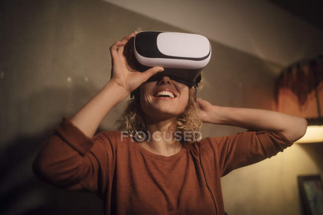 Laughing young woman putting on Virtual Reality Glasses at home — Stock Photo