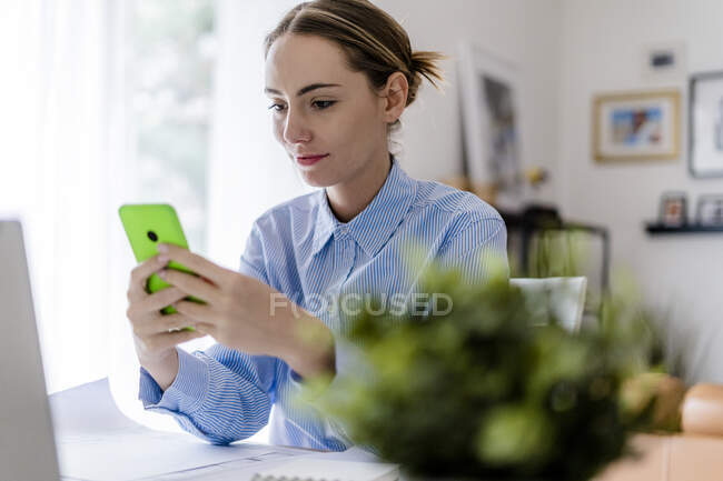 Frau im Büro mit Handy am Tisch — Stockfoto