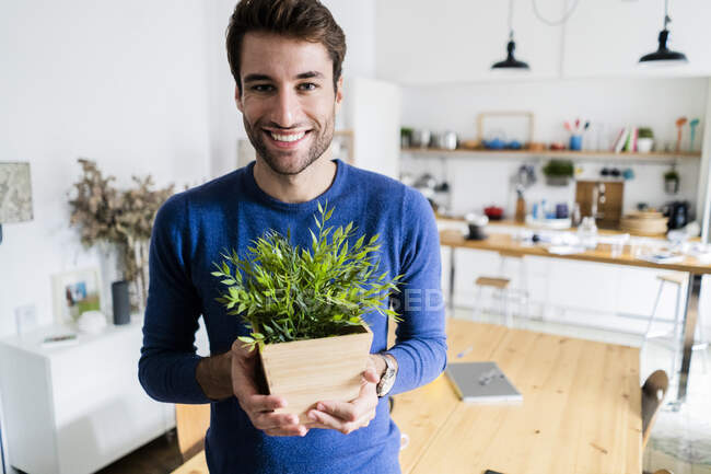 Ritratto di giovane uomo sorridente che tiene la pianta a casa — Foto stock