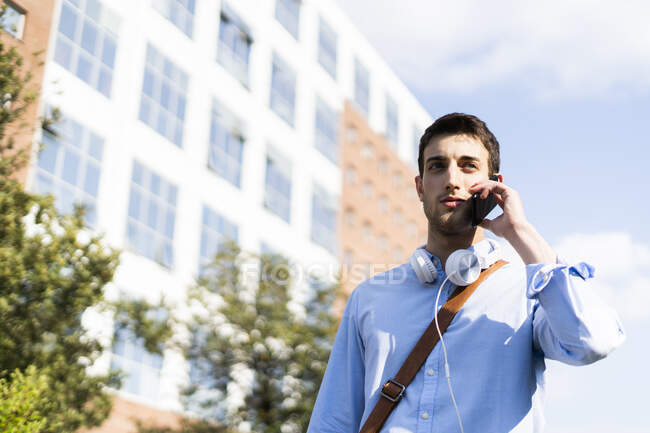 Jovem usando smartphone, fones de ouvido em torno do pescoço na cidade — Fotografia de Stock