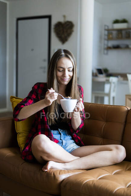 Розслаблена молода жінка їсть зернові у вітальні вдома — стокове фото