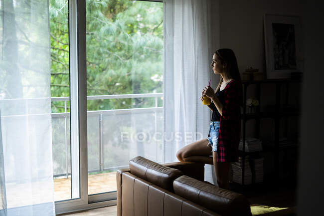 Giovane donna che guarda fuori dalla finestra a casa — Foto stock