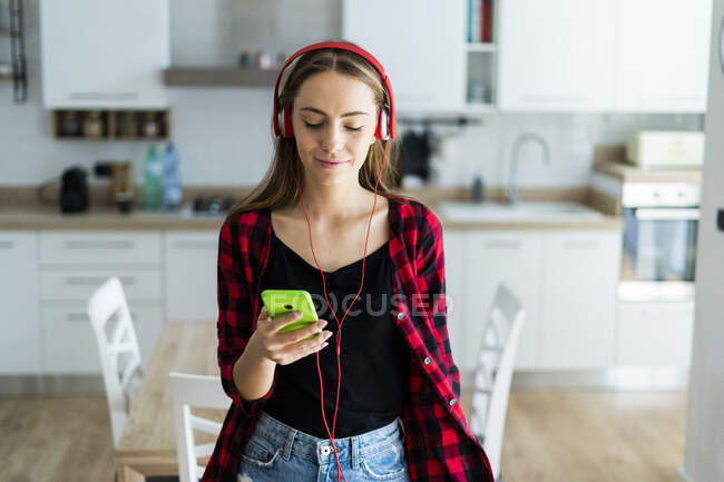 Young woman with cell phone and headphones at home — Stock Photo