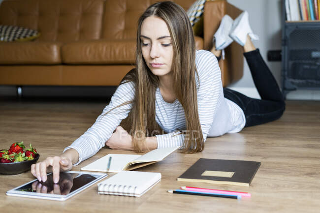 Young woman lying on the floor at home using a tablet — Stock Photo