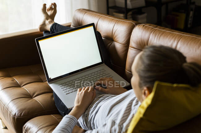 Jeune femme couchée sur le canapé à la maison en utilisant un ordinateur portable — Photo de stock