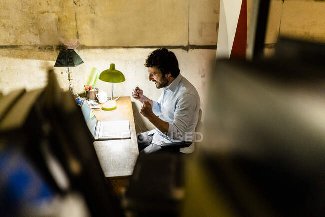 Приветствуя бизнесмена, использующего ноутбук на столе в темноте — стоковое фото