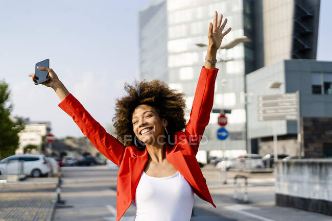 Portrait of happy young woman with smartphone wearing fashionable red suit jacket — Stock Photo