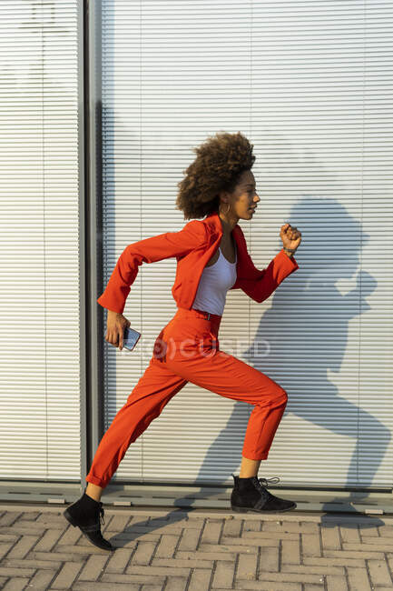 Courir jeune femme avec smartphone portant une combinaison rouge à la mode — Photo de stock