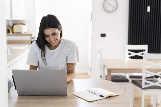 Sorridente giovane donna utilizzando il computer portatile a casa — Foto stock