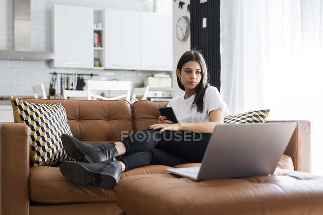 Молода жінка сидить вдома на дивані за допомогою ноутбука. — стокове фото