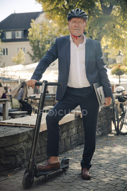 Homme âgé avec e-scooter et ordinateur portable dans la ville — Photo de stock