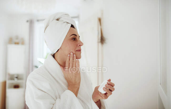 Mulher madura em um banheiro em casa aplicando hidratante — Fotografia de Stock