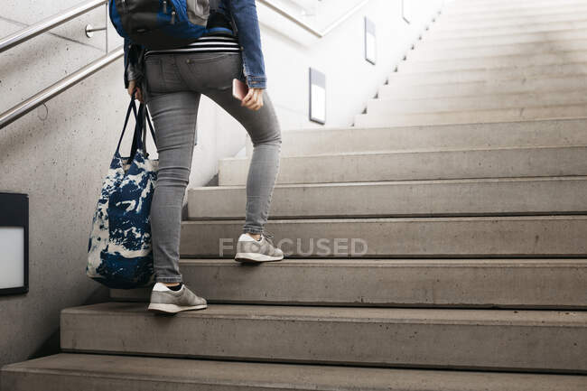 Mulher com saco e mochila subindo escadas na estação — Fotografia de Stock