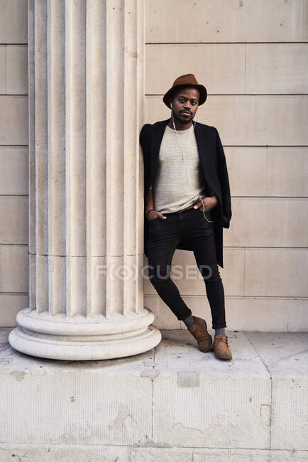 Hombre adulto medio con sombrero marrón, apoyado en la columna - foto de stock