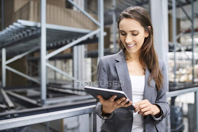 Mujer de negocios sonriente usando tableta en una fábrica - foto de stock