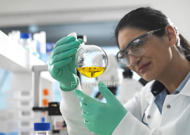 Biotech Research, Científico arremolinando una fórmula química en un frasco de laboratorio durante un experimento - foto de stock