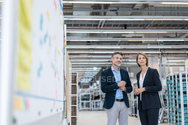 Homme d'affaires et femme d'affaires parlant dans un hall d'usine — Photo de stock