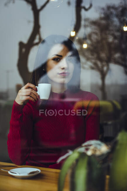 Porträt einer schönen jungen Frau mit einer Tasse Kaffee hinter der Fensterscheibe in einem Café — Stockfoto