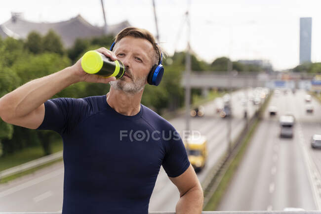 Спортивний чоловік з пляшкою і навушниками на мосту — стокове фото