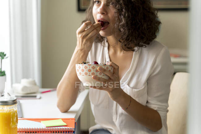 Young woman eating fruit at desk — Stock Photo