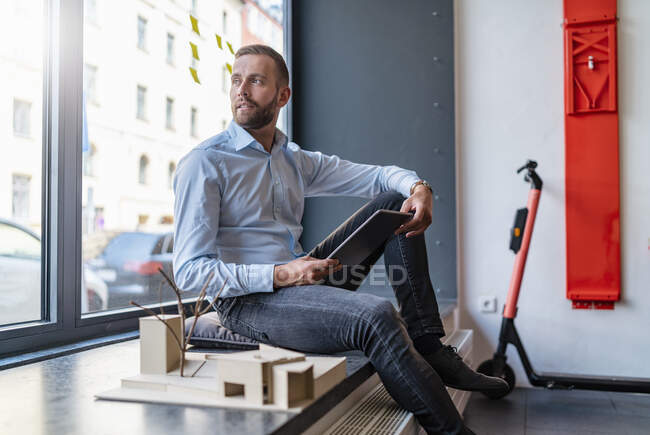 Бізнесмен з планшетом і архітектурним зразком на посаді — стокове фото