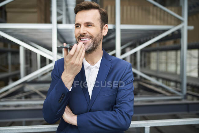Smiling businessman using cell phone in a factory — Stock Photo