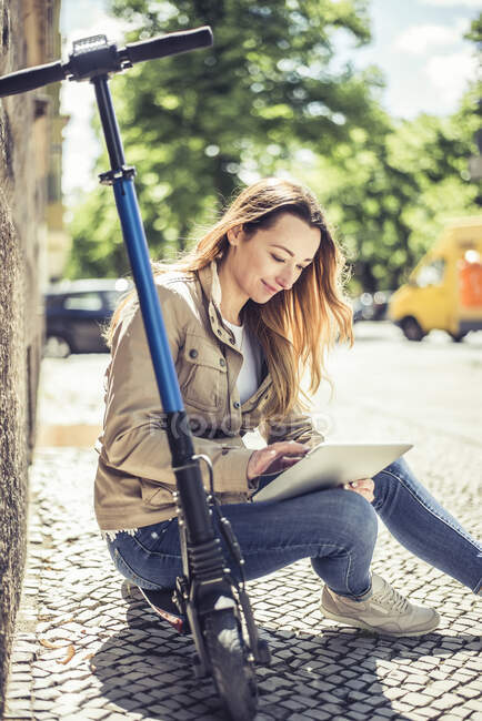 Улыбающаяся женщина сидит на электронном скутере с помощью цифрового планшета — стоковое фото