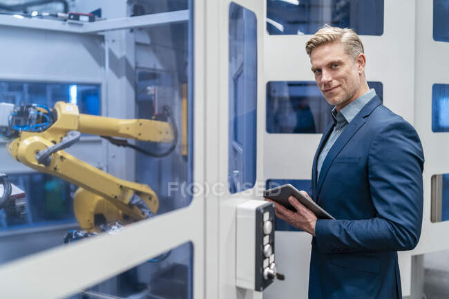 Портрет уверенного бизнесмена перед роботом на современной фабрике — стоковое фото