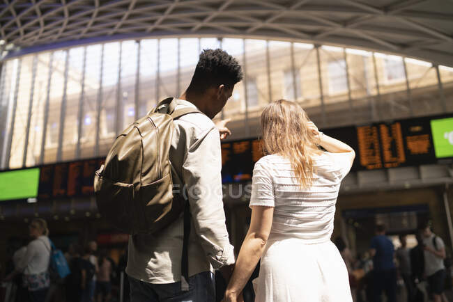 Visão traseira do jovem casal olhando para o painel de exibição da estação ferroviária, Londres, Reino Unido — Fotografia de Stock