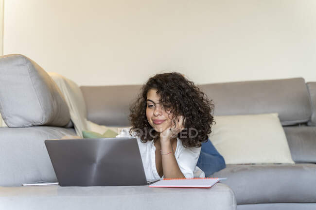 Junge Frau liegt mit Laptop zu Hause auf Couch — Stockfoto