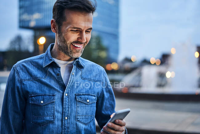 Portrait d'un homme utilisant un smartphone pendant qu'il était en ville le soir — Photo de stock