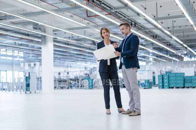 Uomo d'affari e donna d'affari discutono il piano in una sala di fabbrica — Foto stock