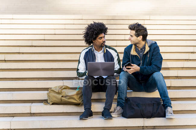 Two casual businessmen sitting on stairs working on laptop — Stock Photo
